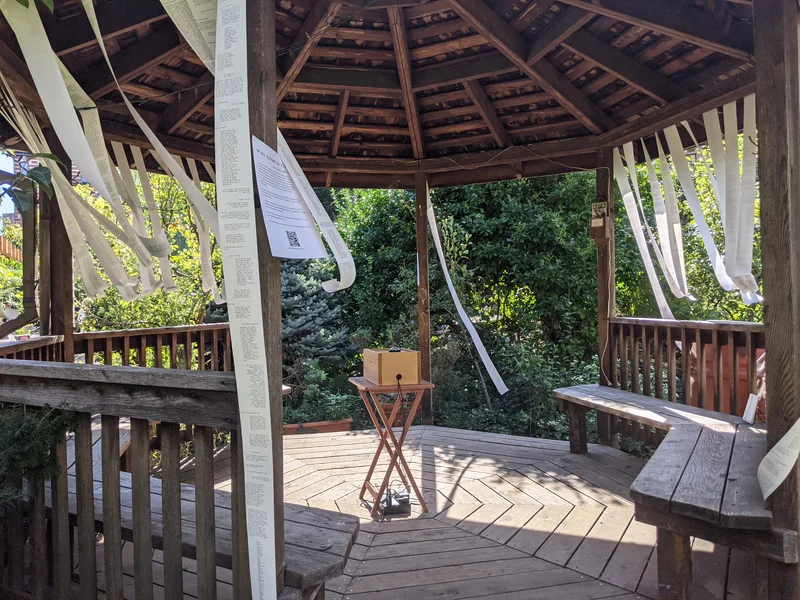 The poetron installed in a garden gazebo surrounded with streamers of receipts blowing in the wind