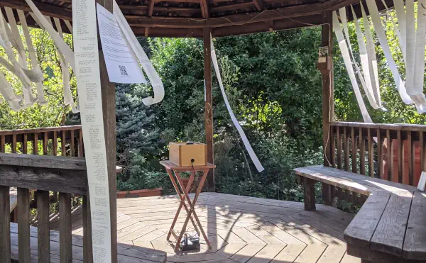 A small wooden box on a table at the center of a gazebo lined with long streamers of receipt paper